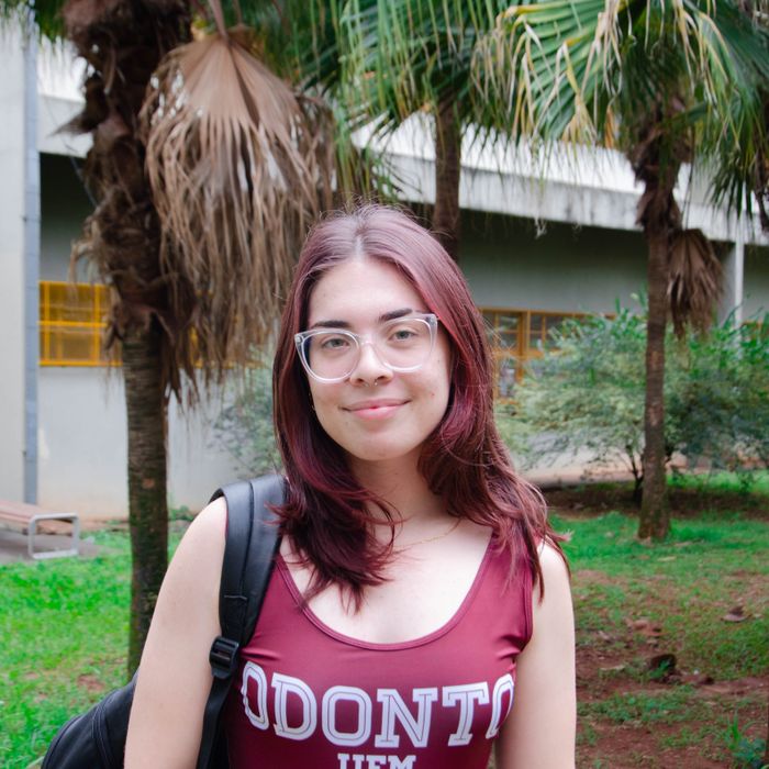 Smiling woman with glasses and red hair stands outdoors among palm trees.