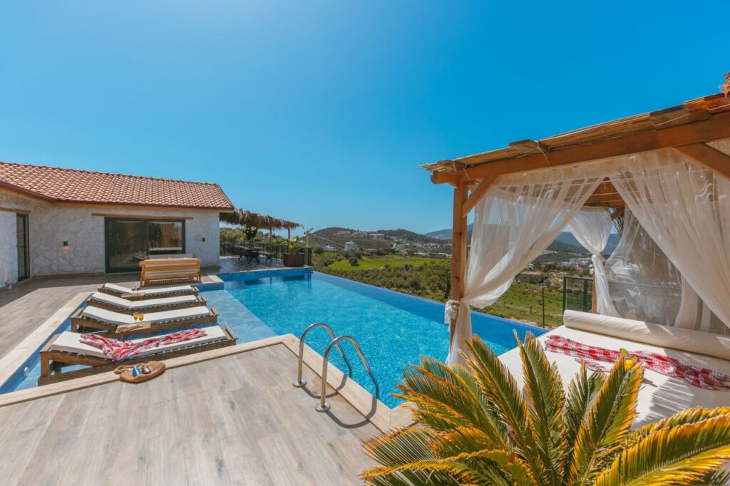 Elegant villa with an infinity pool, deckchairs, and cabana offering a panoramic hillside view.